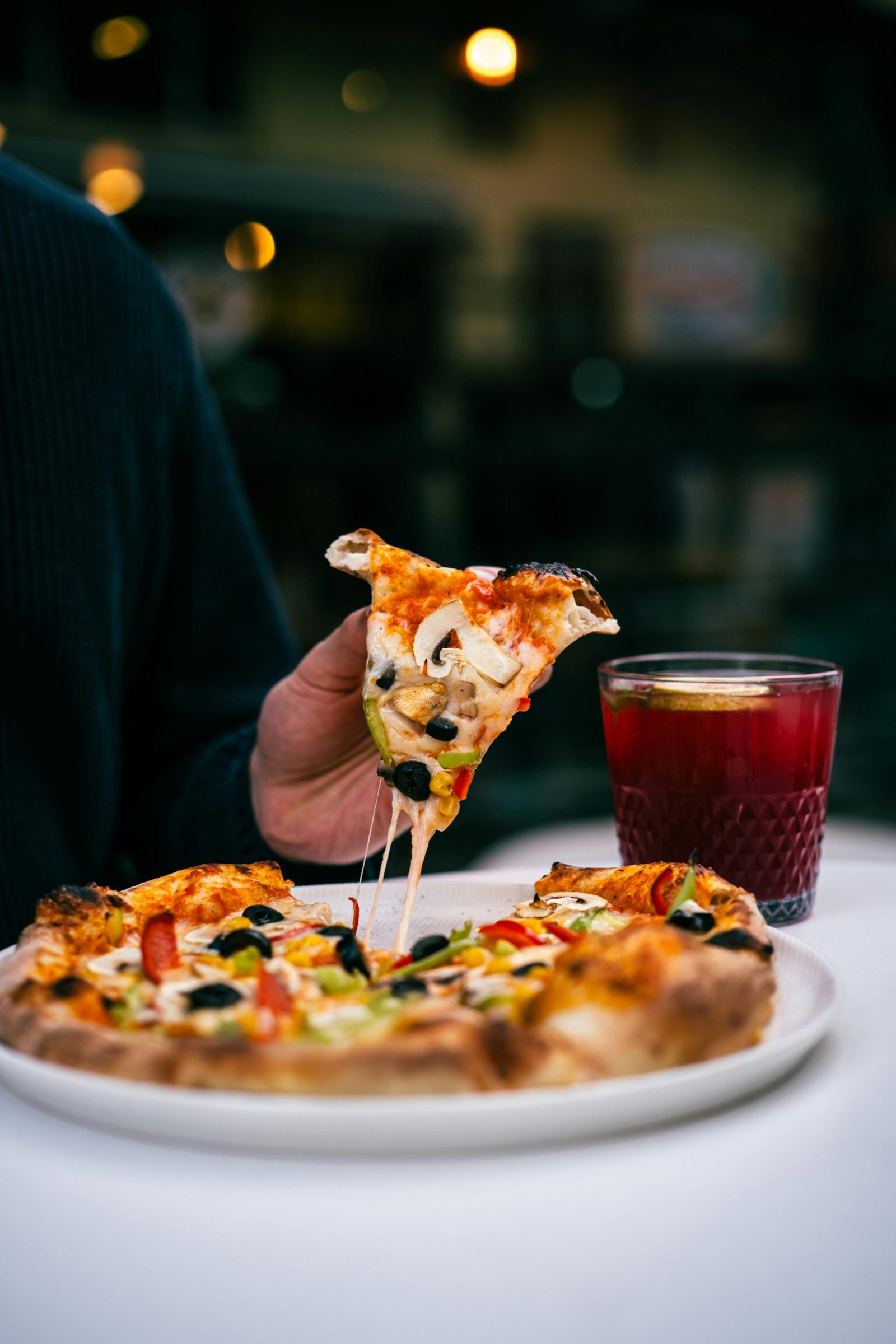 A person enjoying a flavorful slice of vegetarian pizza with a refreshing drink outdoors.
